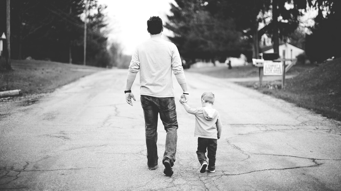 Un hombre camina con su hijo de la mano por una calle asfaltada