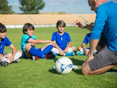 A football coach speaking closely with his youth team, reflecting the importance of connection over competition in early sport