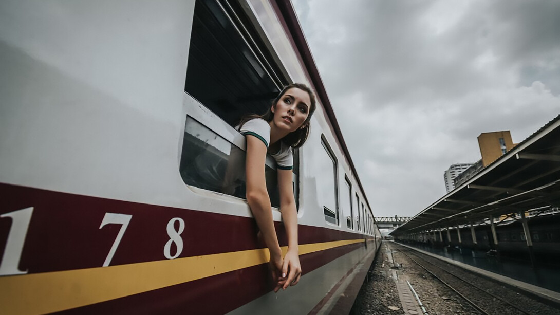 A woman’s head and hands are visible outside a train window under a cloudy daytime sky