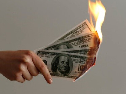 In the midst of the economic crisis, a person holds lighted dollar bills, signifying the alarming financial instability and the potential loss of monetary value