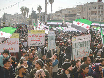 People participate in a mass demonstration, holding signs and flags as they demand rights and political change in Idlib, Idlib Governorate, Syria