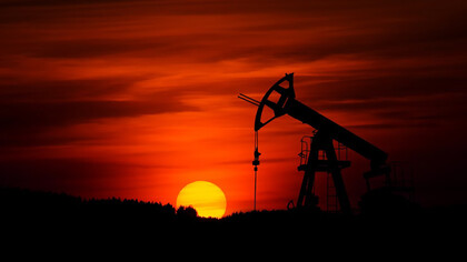 A pump jack extracting crude oil against the backdrop of a sunset