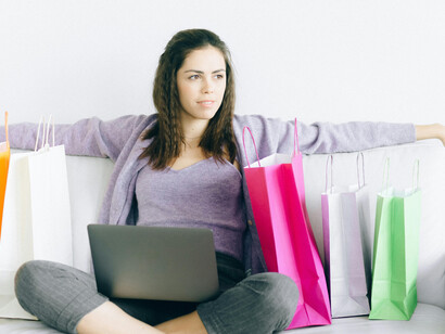 A woman sits on a couch surrounded by paper shopping bags, hinting at shopping addiction