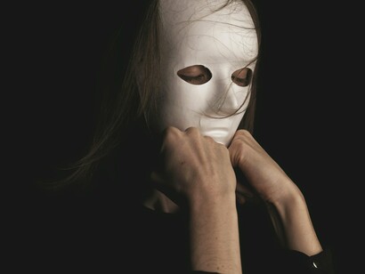 Uma mulher usando uma máscara branca que cobre todo o rosto, deixando apenas os olhos visíveis. Entre radicalismos e discursos fabricados, o artigo sugere uma sociedade onde identidades e consciências parecem cada vez mais ocultas