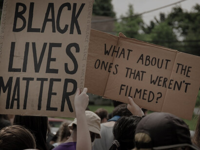 Under the daylight, individuals passionately hold aloft brown wooden signs bearing the profound message "Black Lives Matter"