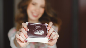 A woman proudly displays her baby's ultrasound photo to the camera