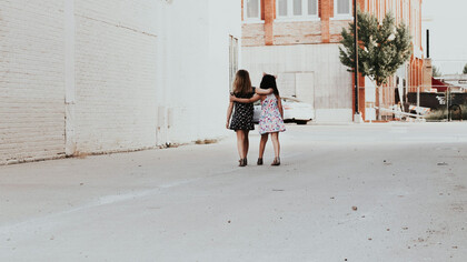 Two girls walk down the street, embracing each other in a warm hug, sharing a moment of kindness and connection