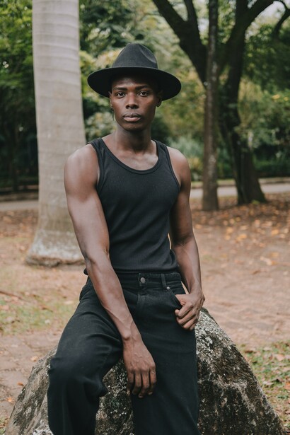 A man wearing a black hat, vest and jeans sitting on a rock