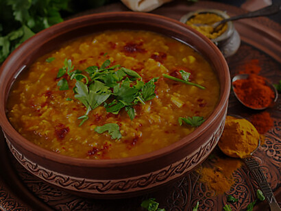 On a rustic black wooden background, a bowl of flavorful traditional Indian dal, a spicy lentil curry, is beautifully displayed, surrounded by an array of fragrant spices and herbs