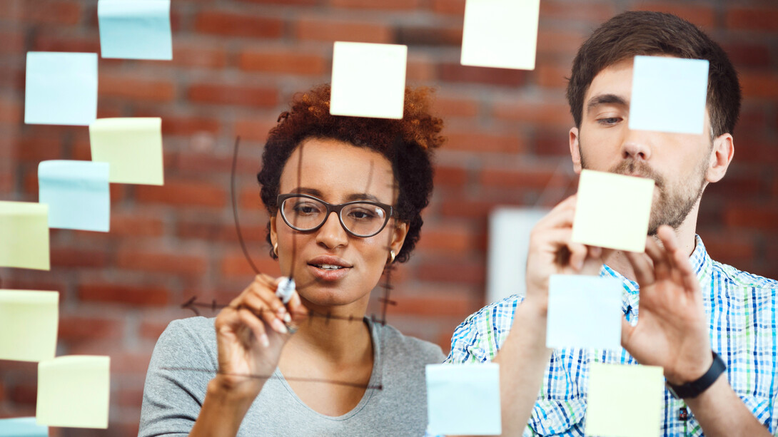 Two colleagues collaborate to brainstorm ideas, using sticky notes to capture each potential solution as they work through the problem-solving process