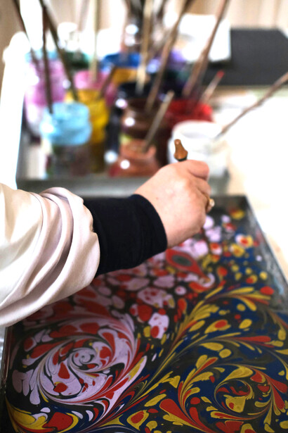 An artist works on colorful Ebru art, surrounded by paints and brushes in a sunlit studio that reflects creativity and craf