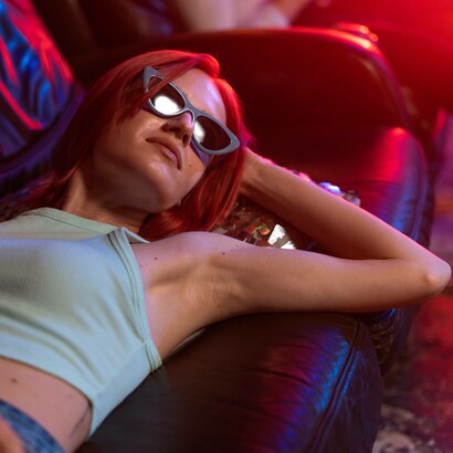 Donna sdraiata su un divano di pelle scuro, illuminata da luci neon rosse e blu, che creano un'atmosfera da discoteca