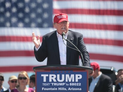 Donald Trump discursa em comício no Arizona, Estados Unidos (2016), usando boné com o slogan "Make America Great Again". Trump reclama ter cunhado o slogan em 2014, colou-o a si, ritmou e iconografou com ele as campanhas, as vitórias e repete-o à exaustão

