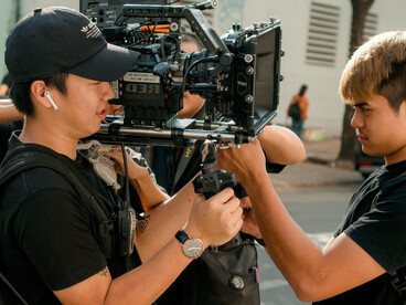 Photo of a movie crew standing together behind the scenes, with film cameras, lights, and action equipment in view