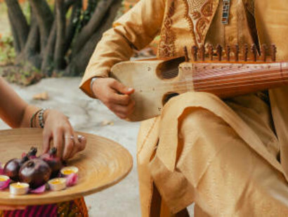An Indian musician in traditional attire plays the sitar outdoors during a festive celebration at home, while a woman in a saree lights a diya lamp for Diwali