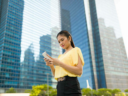 An Asian woman reading text messages while sitting outside
