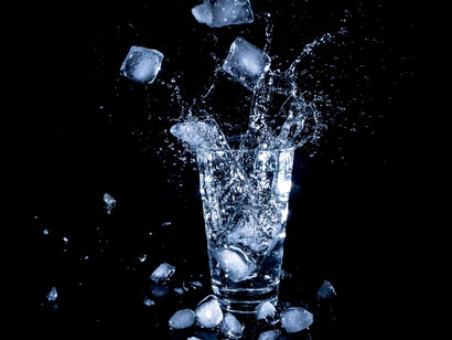 A tall glass of water with ice cubes falling in it