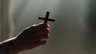 Una mano sostiene una cruz bajo un halo luminoso