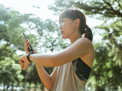 A woman checking her smartwatch while holding a smartphone outdoors, symbolizing the growing connection between personal health monitoring and digital technology