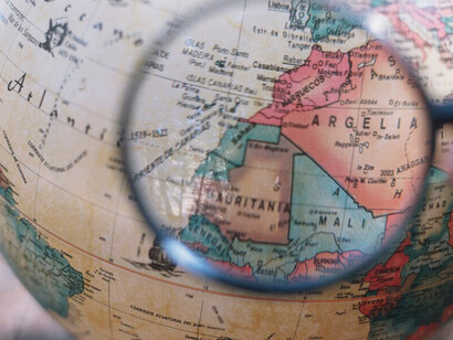 An individual studying a globe through a magnifying glass, highlighting a quest for understanding international relations and geographical complexities