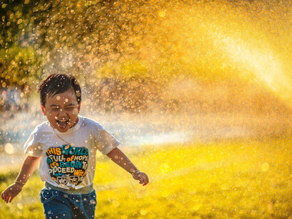 A child joyfully plays in sprinklers