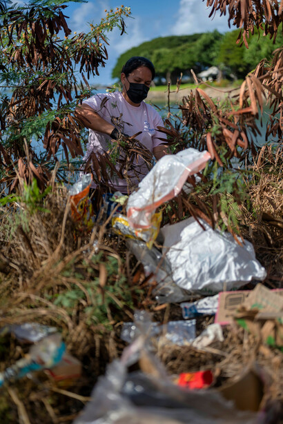 A scene of severe plastic pollution in Myanmar, with debris scattered among trees and floating in the river