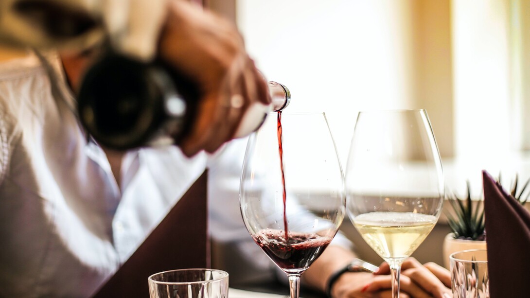 Garçom serve vinho tinto em taça ao lado de vinho branco