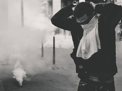 In the midst of chaos and unrest on the streets of Lyon, France, a brave man stands with his face covered, using his shirt as protection against the tear gas grenades fired by the police during the 25th weekend of Yellow Vest protests