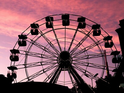 A photo capturing the silhouettes of a Ferris wheel and a carousel at dusk, set against a soft pink sky at the fair
