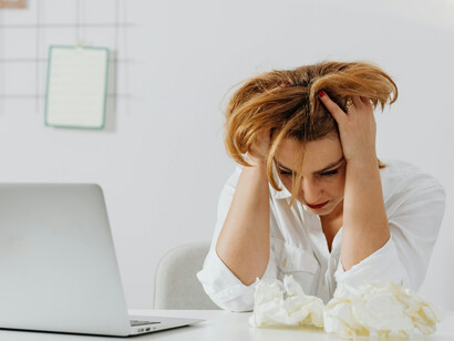 A woman in a white long-sleeved shirt appears stressed and is crying at work