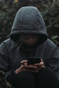 A person sitting on a rock, staring at their phone, surrounded by a sense of grief and the haunting presence of technology