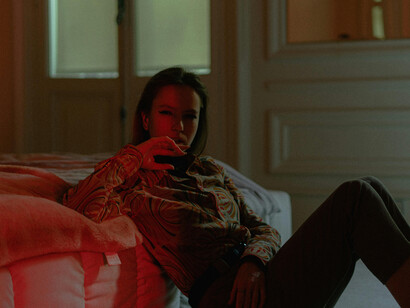 In the stillness of a dark room, a woman rests against her bed, embodying silence and solitude