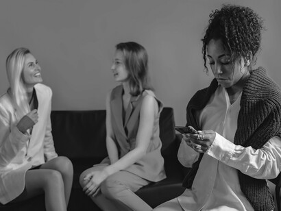 Sentada ao lado de outras pessoas, a mulher parece mergulhada em seu próprio universo. O uso excessivo das redes sociais pode transformar momentos de convivência em experiências marcadas pela distância e pelo isolamento