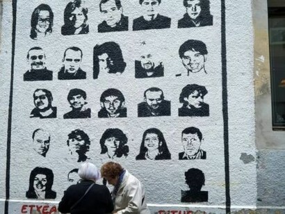 Dos mujeres charlan ante un mural con los rostros de miembros de ETA
