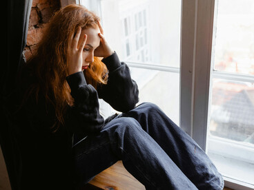 Stressed woman sitting on a window sill, lost in thought