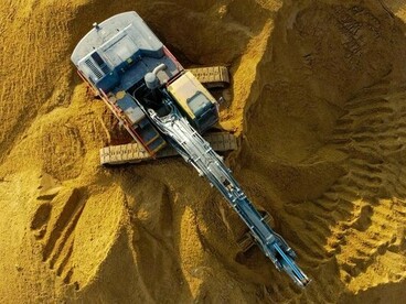 Earthmoving machinery working across a sandy rise, representing the process of preparing ground for structures