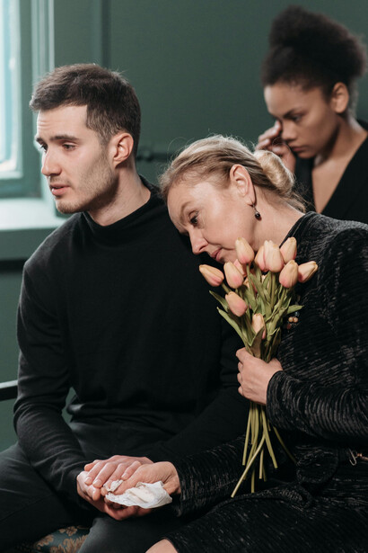 A mother, overwhelmed with grief, clings to her son as they attend a solemn funeral service