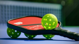 A pickleball paddle with four pickleballs, ready for a game on a sunny court