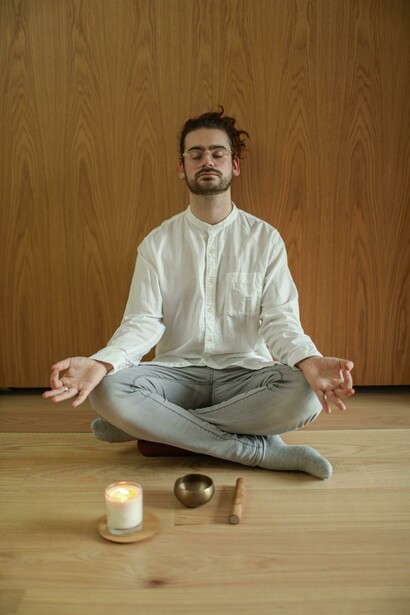 An adult man practices meditation indoors with a lit candle and a singing bowl, embracing mindfulness and inner calm in a quiet reflective space