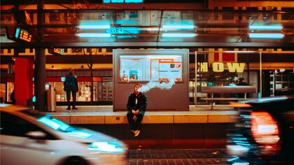 A man sitting at a bus stop and vaping, reflecting how people often turn to vaping as a way to cope with stress or anxiety in an increasingly hectic world