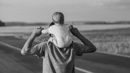 Pai caminha na praia com o seu filho sob os ombros