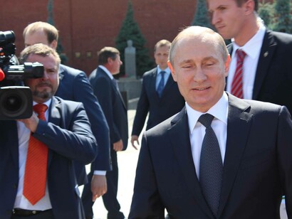 Russian President Vladimir Putin smiles as he is followed by a cameraman as he prepares his next war move with Ukraine