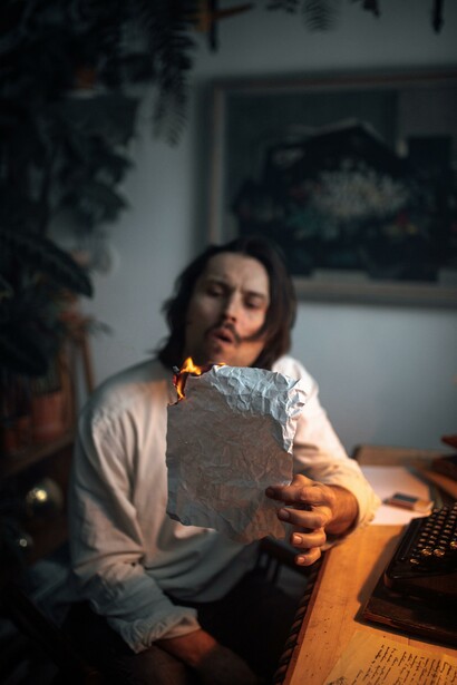 A poet burning a piece of paper at his desk 