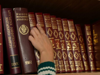 Pessoa seleciona livro de enciclopédia em uma prateleira. "O senhor entende que uma História paralela desse nível alteraria completamente o mundo, não. M. Rélleivaux? Não bastaria apenas criar situações com características egípcias (na arquitetura ou no vestir, por exemplo): as mudanças seriam muito mais profundas. A esta hora certamente não estaríamos conversando em francês – acredito que nem existiria, pelo menos não como o conhecemos –, mas em alguma língua que possivelmente usasse versões modernas de hieróglifos e viria do copta, não do latim ou do grego"
