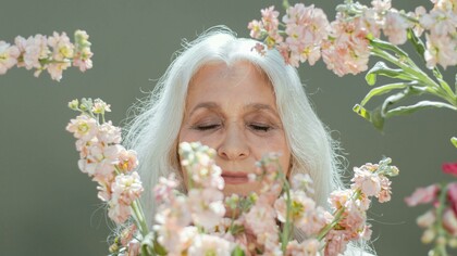 A woman with white hair surrounded by white and pink flowers, symbolizing healthy aging and longevity