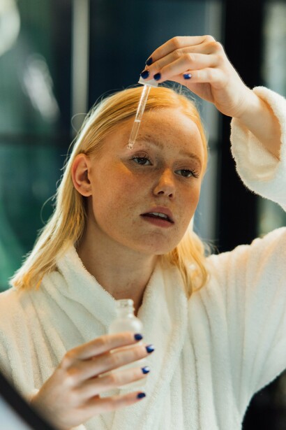 A woman in a white robe carefully applying serum, reflecting the importance of delivering skincare ingredients to the skin in the right way