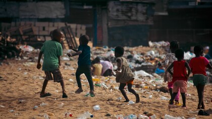 Children play on a waste-covered urban beach, highlighting the growing problem of environmental pollution