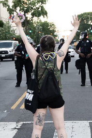 A woman in a green and black tank top raises her hands in protest