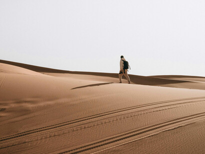 A lone silhouette moving through an endless desert, surrounded by a wide, untamed wilderness