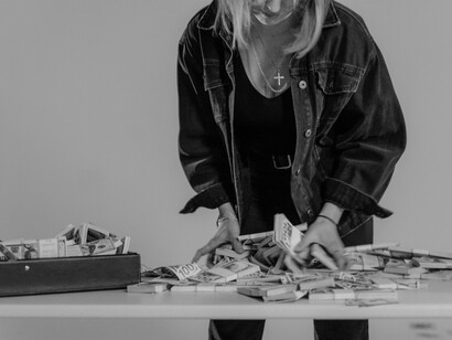 Uma mulher manuseia maços de dinheiro dentro de uma mala preta. A fotografia remete aos escândalos financeiros e à percepção pública de falta de responsabilização abordados no texto